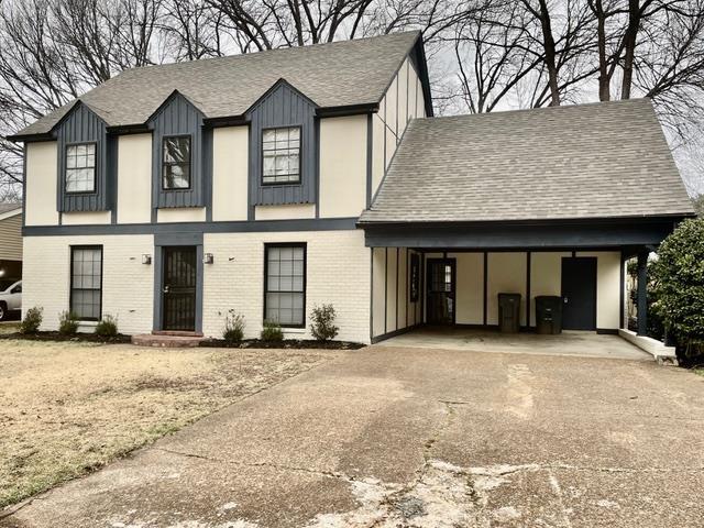 tudor home featuring board and batten siding, brick siding, driveway, and roof with shingles