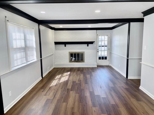 unfurnished living room featuring a fireplace, beamed ceiling, baseboards, and wood finished floors