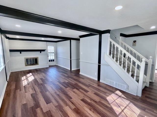 unfurnished living room featuring visible vents, stairway, a brick fireplace, wood finished floors, and beamed ceiling