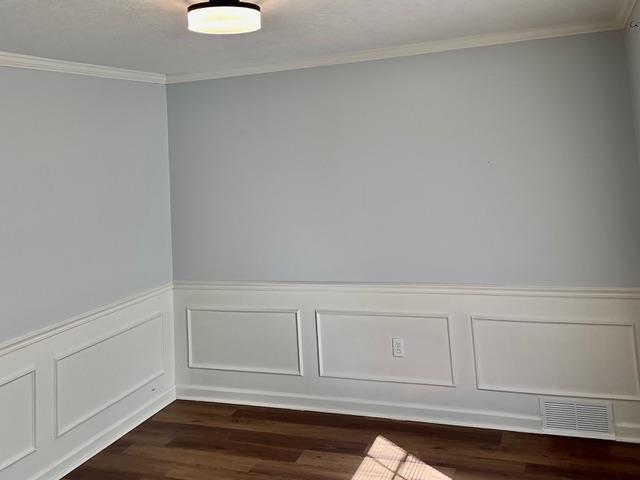 spare room featuring dark wood-style floors, ornamental molding, wainscoting, and visible vents