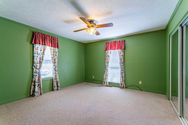 carpeted empty room with a textured ceiling, plenty of natural light, and a ceiling fan