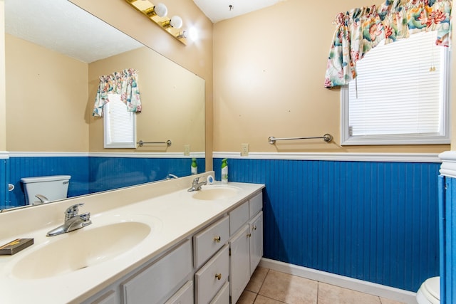 full bath with tile patterned flooring, wainscoting, a sink, and toilet