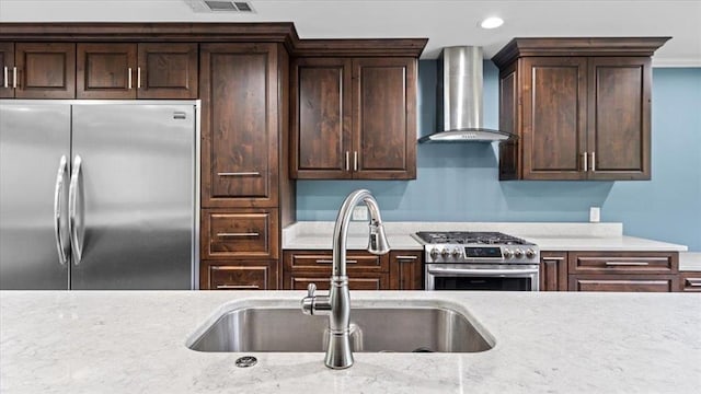 kitchen with dark brown cabinetry, recessed lighting, a sink, appliances with stainless steel finishes, and wall chimney range hood