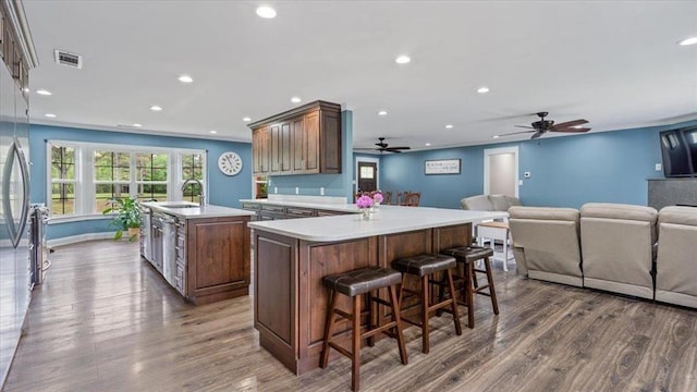 kitchen featuring dark wood-style flooring, light countertops, visible vents, a kitchen island with sink, and a sink