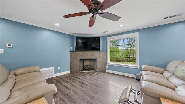 living room with a fireplace, crown molding, visible vents, wood finished floors, and baseboards