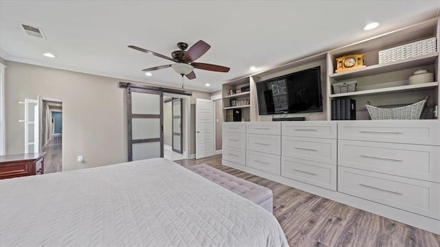 bedroom with recessed lighting, visible vents, light wood-style flooring, a barn door, and ornamental molding