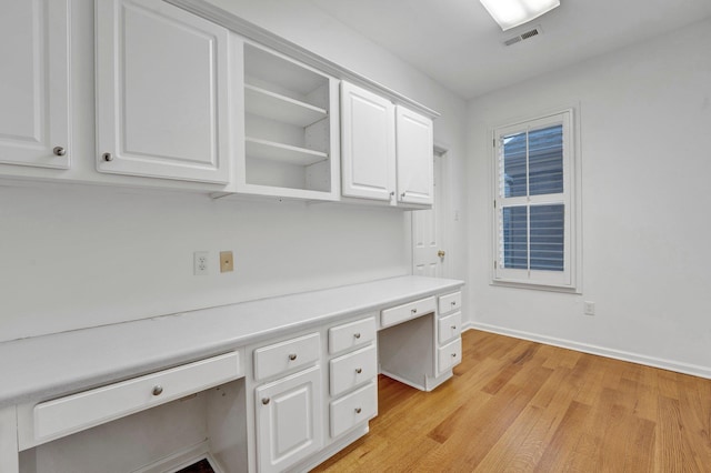 unfurnished office featuring baseboards, light wood-style flooring, visible vents, and built in desk