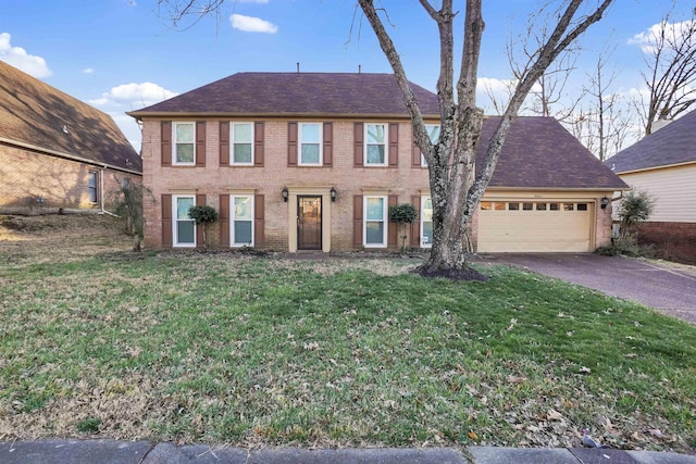 colonial inspired home featuring aphalt driveway, an attached garage, brick siding, roof with shingles, and a front yard