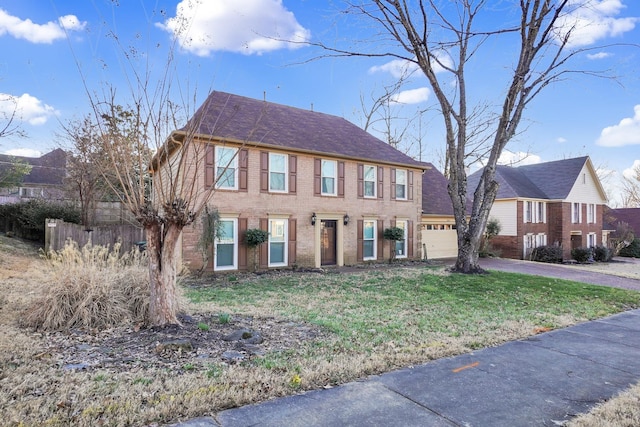 colonial house with an attached garage, fence, aphalt driveway, and brick siding