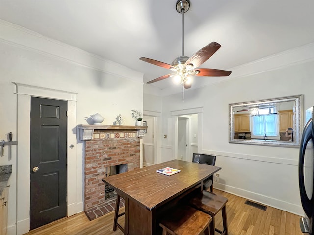 dining space with light wood-type flooring, visible vents, a fireplace, and ornamental molding