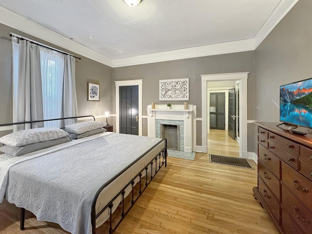 bedroom with light wood-style floors, a fireplace, baseboards, and crown molding