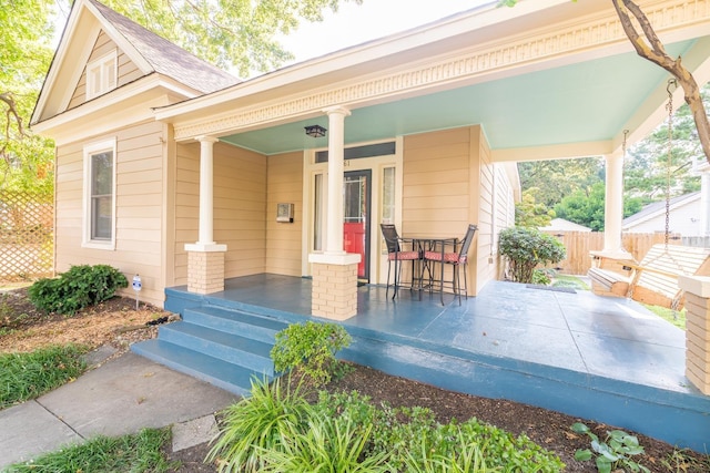 entrance to property featuring covered porch, a shingled roof, and fence