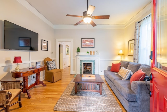 living area with light wood-style floors, a fireplace, ornamental molding, and a ceiling fan