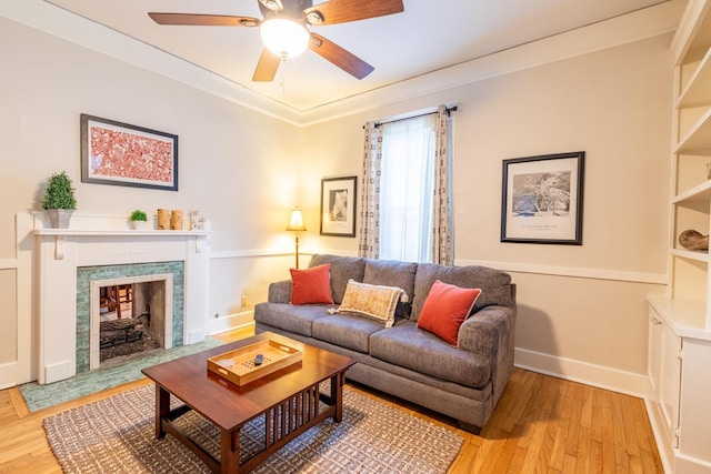 living room with baseboards, a ceiling fan, light wood-style flooring, crown molding, and a high end fireplace