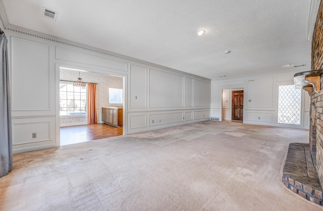 unfurnished living room featuring light carpet, visible vents, a decorative wall, and ornamental molding