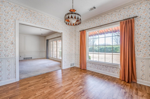 unfurnished room with wallpapered walls, visible vents, ornamental molding, and wainscoting