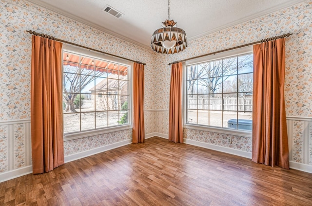 unfurnished dining area featuring wallpapered walls, visible vents, wainscoting, wood finished floors, and a textured ceiling