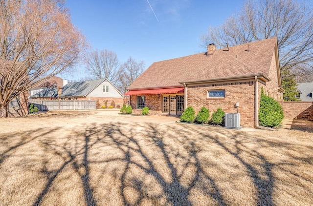 back of house featuring central AC, brick siding, fence, french doors, and a chimney