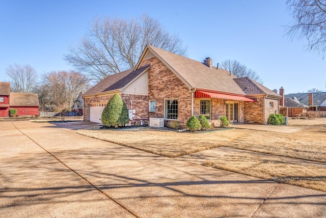 view of home's exterior with concrete driveway, a chimney, an attached garage, central AC, and brick siding