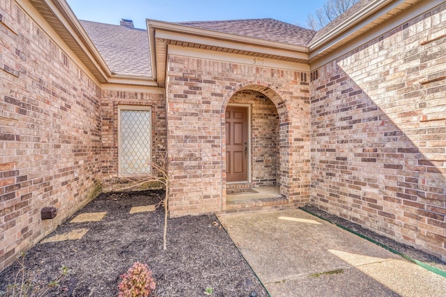 view of exterior entry featuring a shingled roof and brick siding