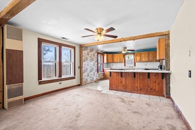 kitchen with light carpet, a peninsula, visible vents, tile counters, and brown cabinets