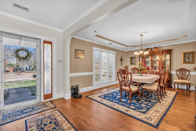 dining space with visible vents, a raised ceiling, wood finished floors, crown molding, and a chandelier