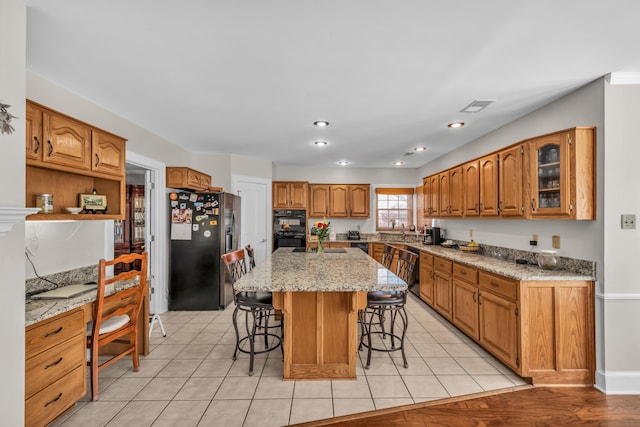 kitchen with visible vents, brown cabinetry, a center island, black appliances, and a kitchen bar