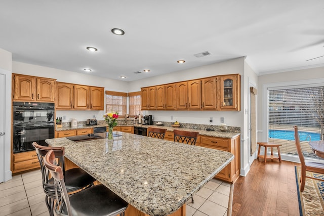 kitchen with light stone counters, a kitchen island, visible vents, a kitchen breakfast bar, and brown cabinetry