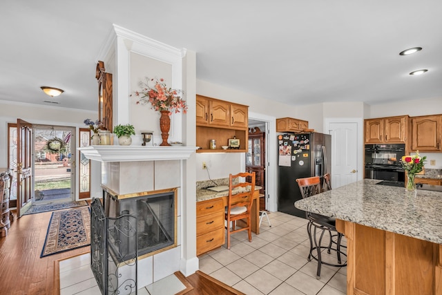 kitchen with dobule oven black, stainless steel fridge, a kitchen breakfast bar, light stone countertops, and crown molding