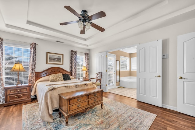 bedroom with a tray ceiling, wood finished floors, visible vents, and baseboards