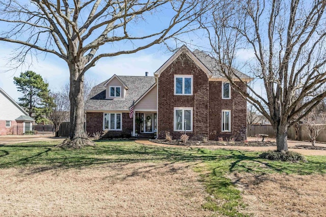 traditional-style home featuring a front yard, fence, and brick siding