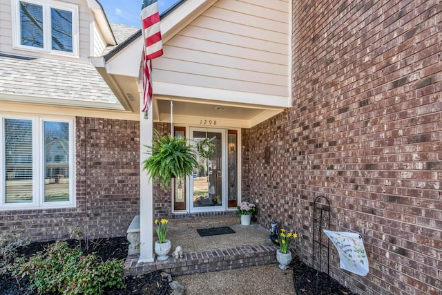 property entrance featuring a shingled roof and brick siding