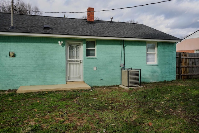 rear view of house with roof with shingles, brick siding, a chimney, a lawn, and fence