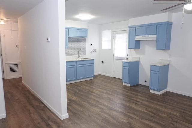 kitchen with tasteful backsplash, visible vents, under cabinet range hood, blue cabinetry, and a sink