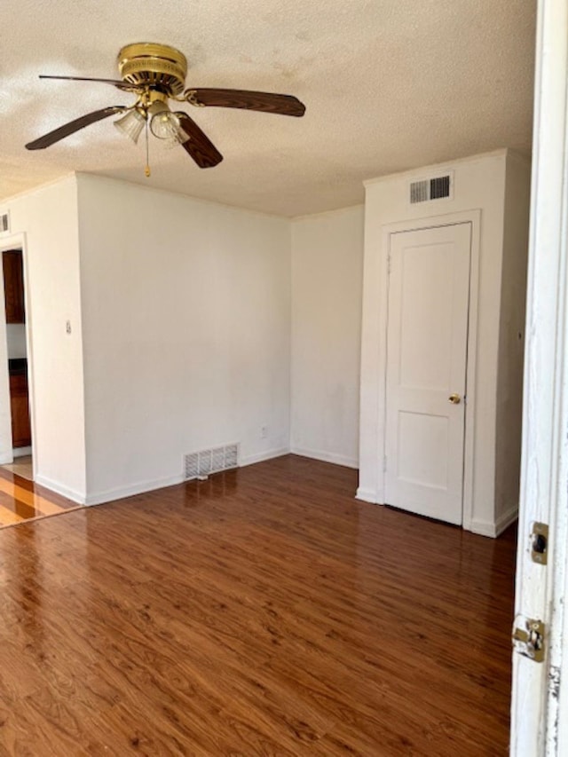 empty room featuring a textured ceiling, visible vents, and wood finished floors