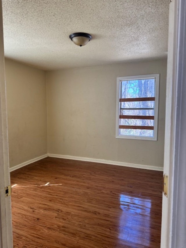 unfurnished room with a textured ceiling, baseboards, and wood finished floors