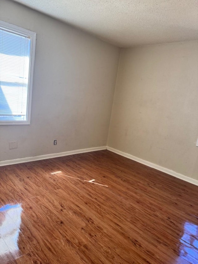 empty room with a textured ceiling, wood finished floors, and baseboards