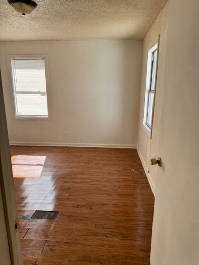 spare room with a textured ceiling, baseboards, and wood finished floors