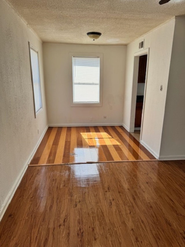 empty room with a textured ceiling, baseboards, and wood finished floors