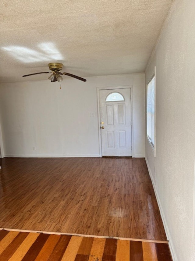 foyer entrance with a textured wall, a textured ceiling, baseboards, and wood finished floors