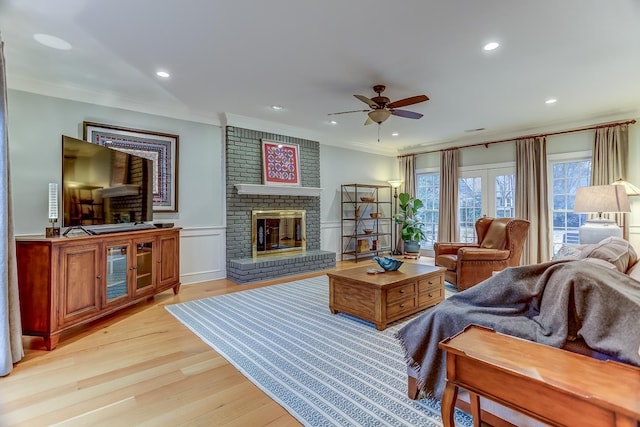 living area featuring wainscoting, ornamental molding, a fireplace, and light wood-style floors