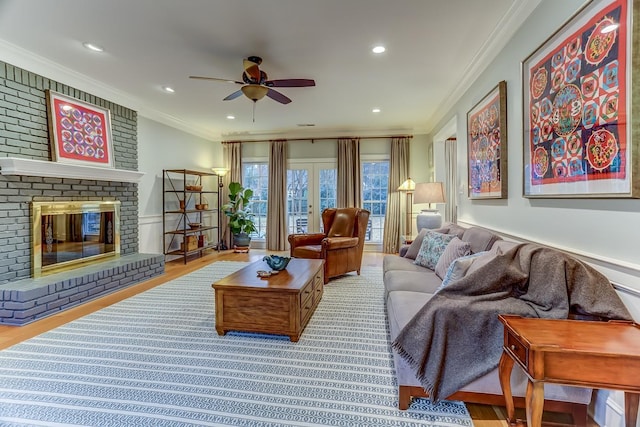 living room with recessed lighting, wood finished floors, a ceiling fan, ornamental molding, and a brick fireplace