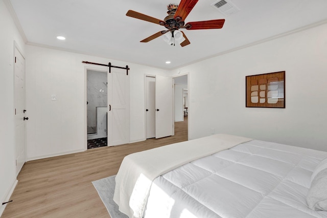 bedroom with a barn door, visible vents, light wood-style flooring, ornamental molding, and recessed lighting