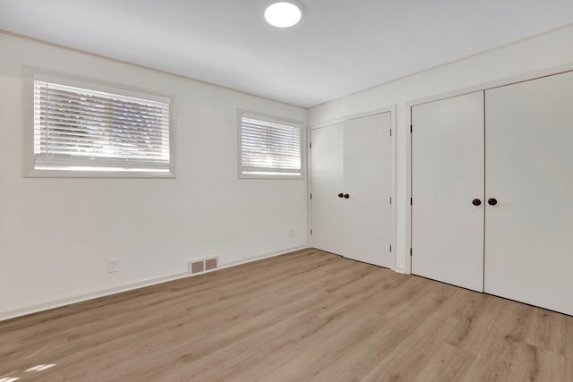 unfurnished bedroom featuring light wood-style flooring, visible vents, and two closets