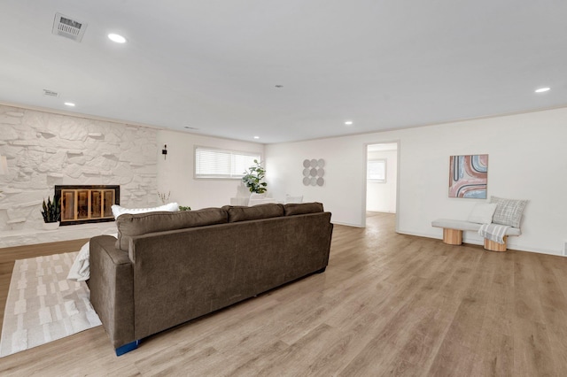 living room featuring light wood-style flooring, recessed lighting, visible vents, and a stone fireplace