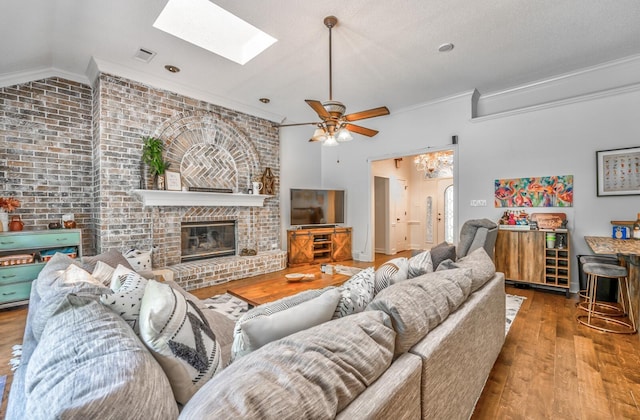 living area featuring vaulted ceiling with skylight, visible vents, ornamental molding, wood finished floors, and a fireplace