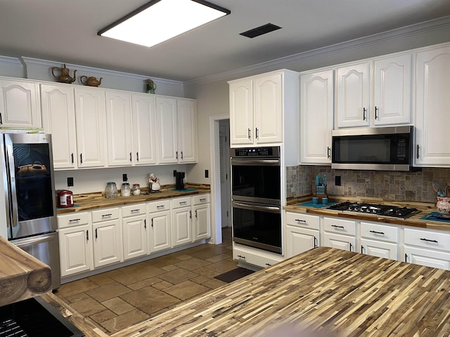 kitchen featuring stone tile floors, butcher block counters, appliances with stainless steel finishes, ornamental molding, and white cabinetry