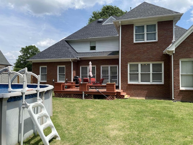 rear view of property featuring a shingled roof, brick siding, a yard, and a deck