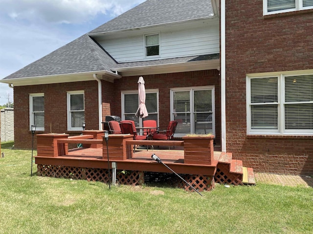 back of house with a deck, brick siding, a lawn, and a shingled roof