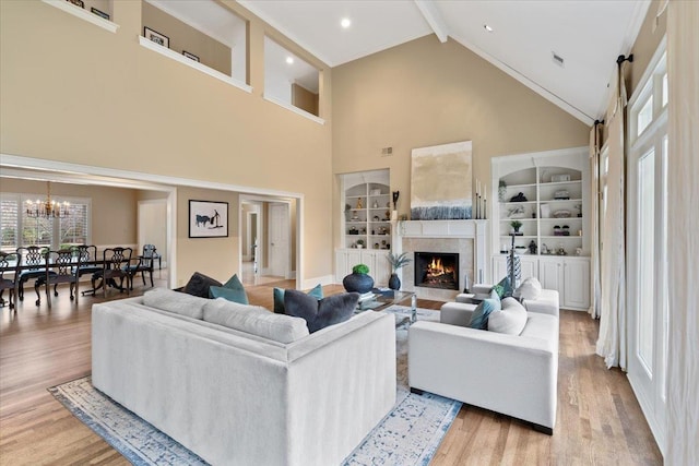 living area featuring built in features, a tile fireplace, light wood-style floors, a chandelier, and beam ceiling